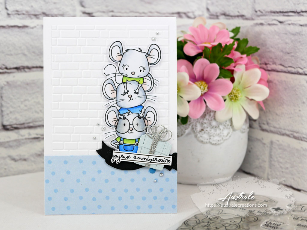 Carte d'anniversaire avec fond embossé mur de briques, petites souris et paquet cadeau dans un combo en vert, blanc et bleu.