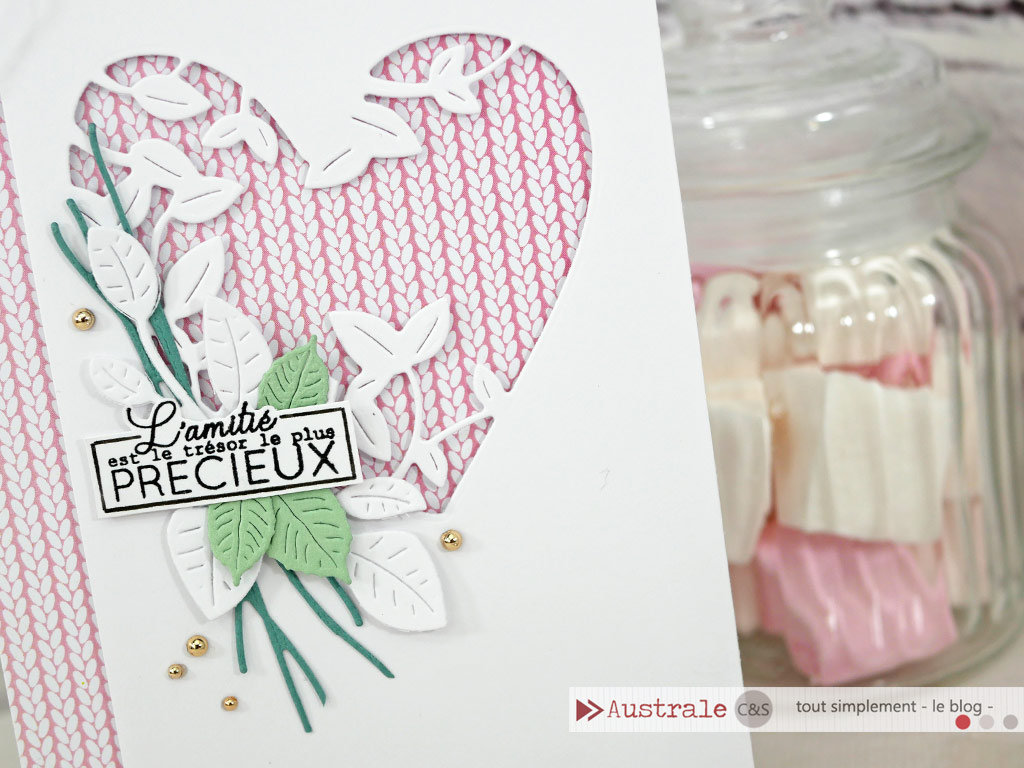 Carte d'amitié pour la Saint Valentin en rose, blanc, cuivré, une touche de feuillages et de couture, un coeur évidé sur fond de tricot rose et étiquette pour le sentiment.